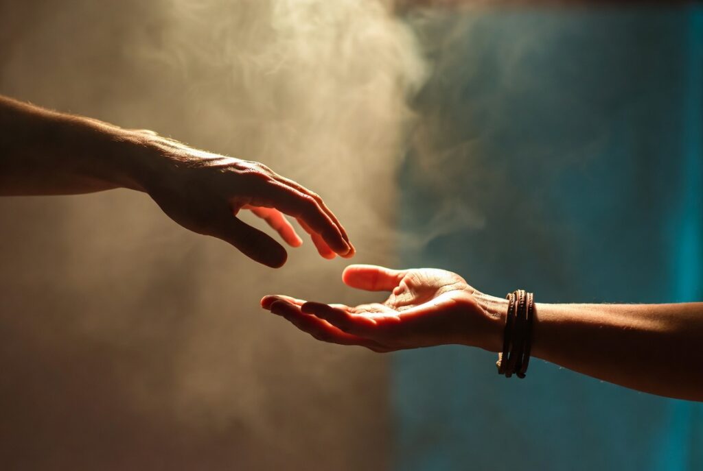 Two hands reaching toward each other, one with a leather bracelet, symbolizing repair and reconnection in relationships